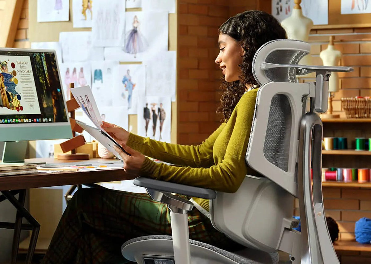 Designer reading sketches in an HBADA X7 smart ergonomic chair in a sunny studio