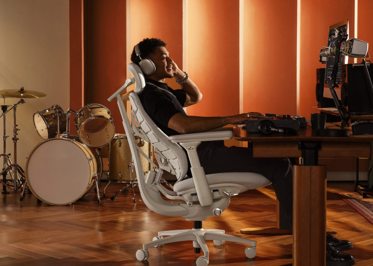 Music producer in headphones leaning back in a white LiberNovo Omni chair in a warm studio
